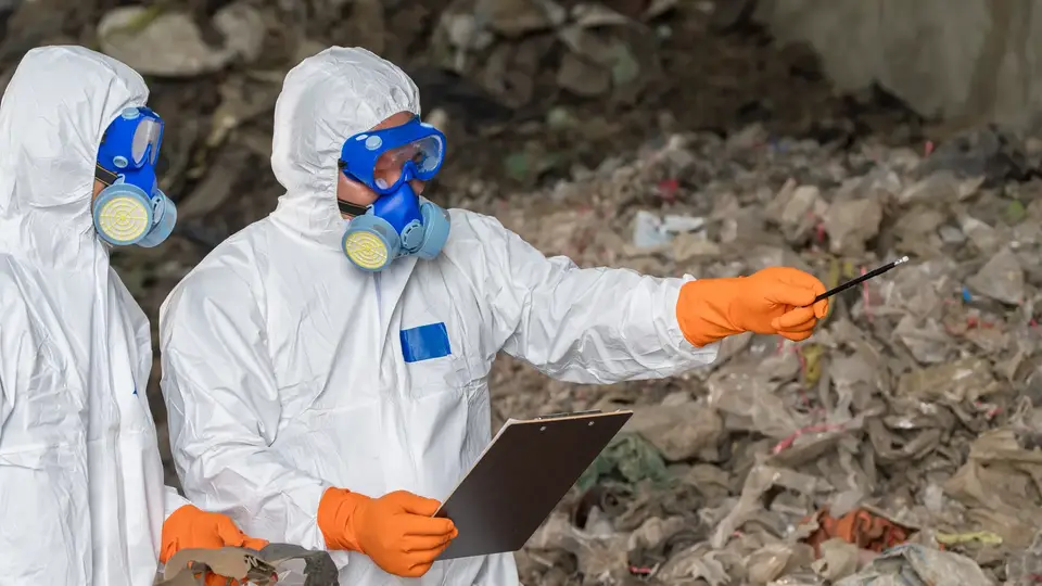 Asbestos surveyors in protective equipment recording sample details on a clipboard